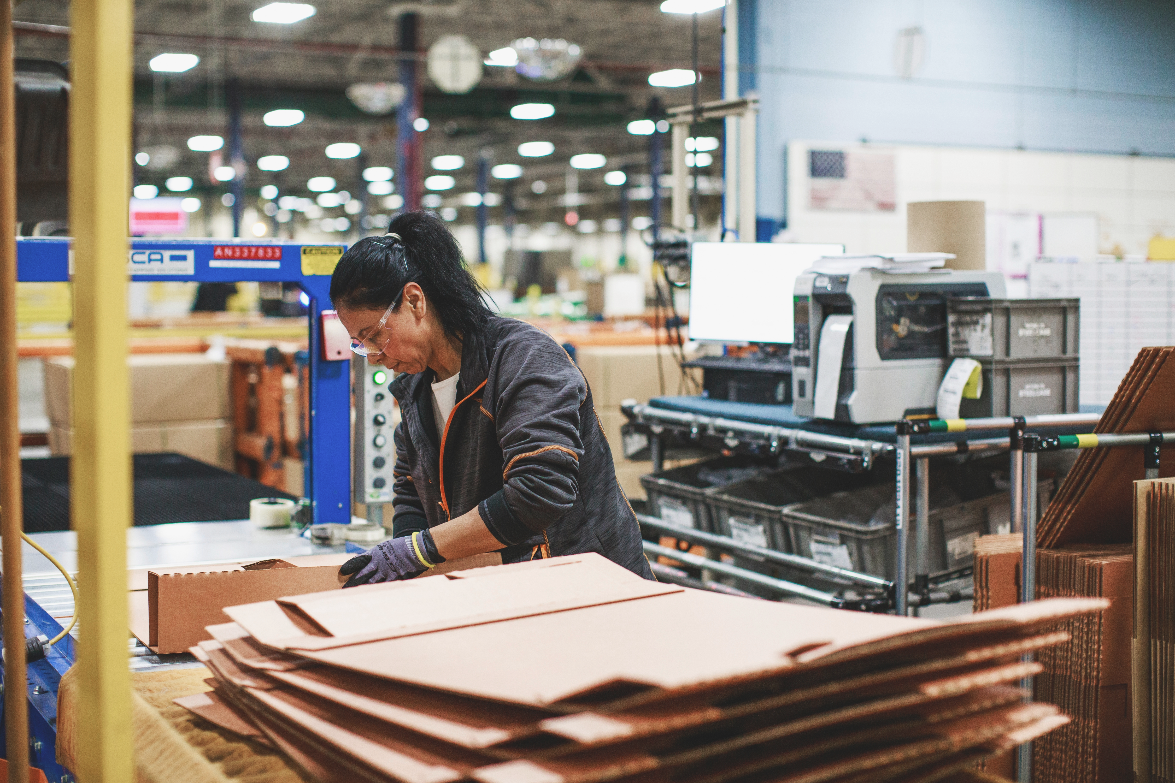 Woman in manufacturing setting folding recyclable cardboard to be used in packaging